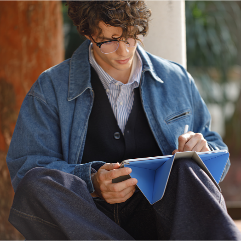 Person sitting outdoors, writing in a notebook with a blurred background